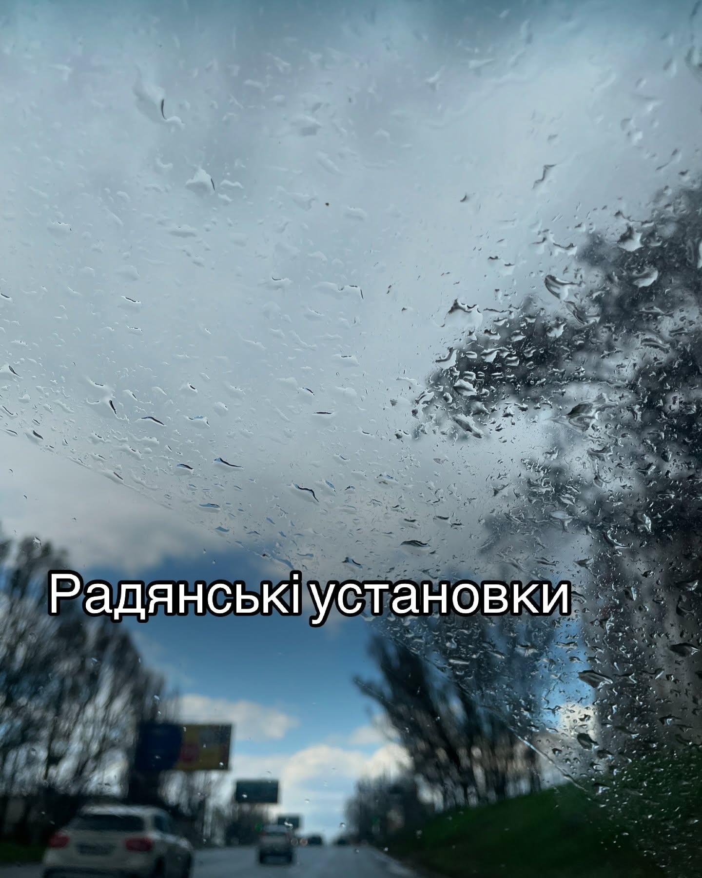 Дощові краплі на склі автомобіля, за ним дорога і дерева; напис «Радянські установки»