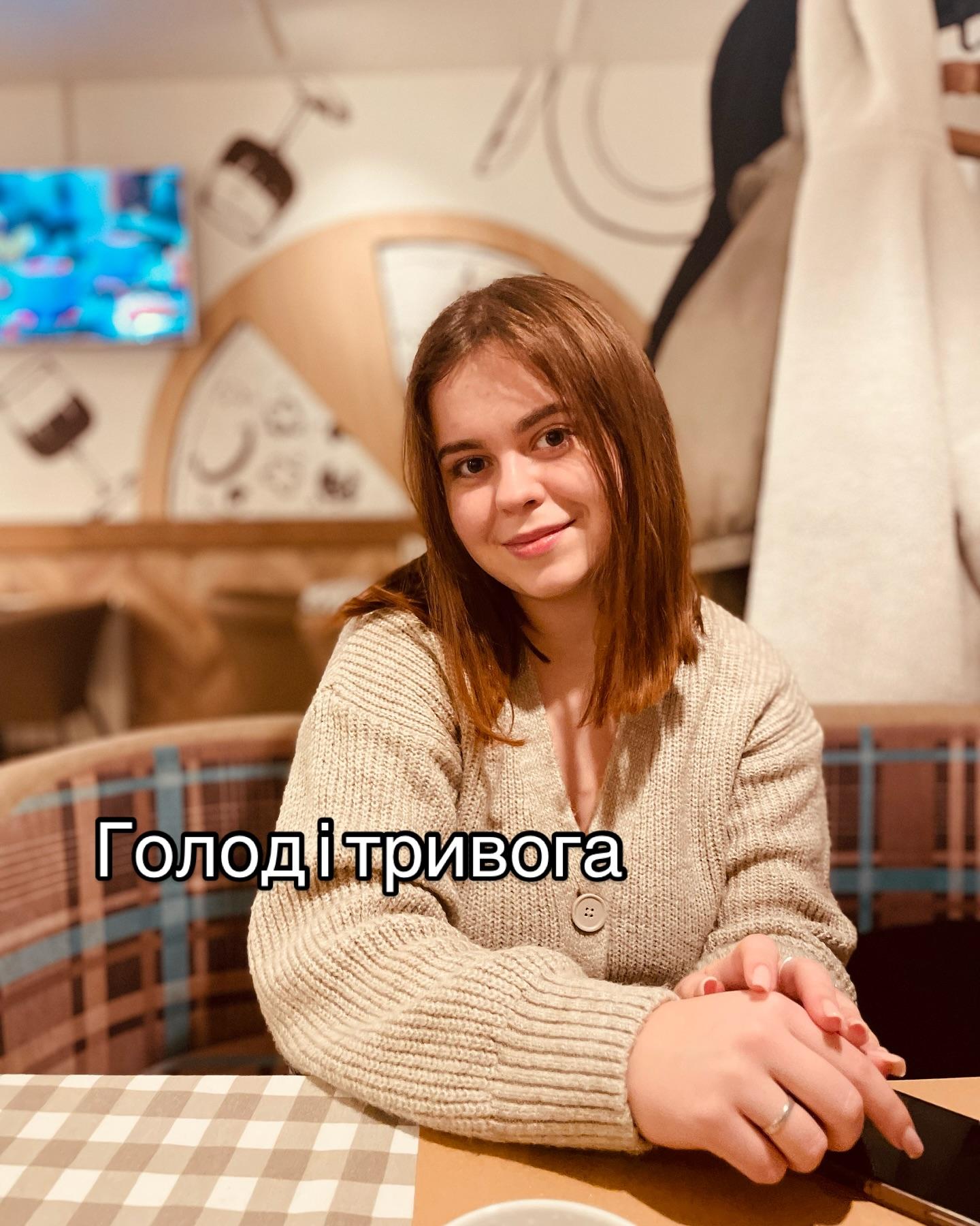 Марія Дерев'янченко в бежевому светрі сидить за столиком у кафе; напис «Голод і тривога»