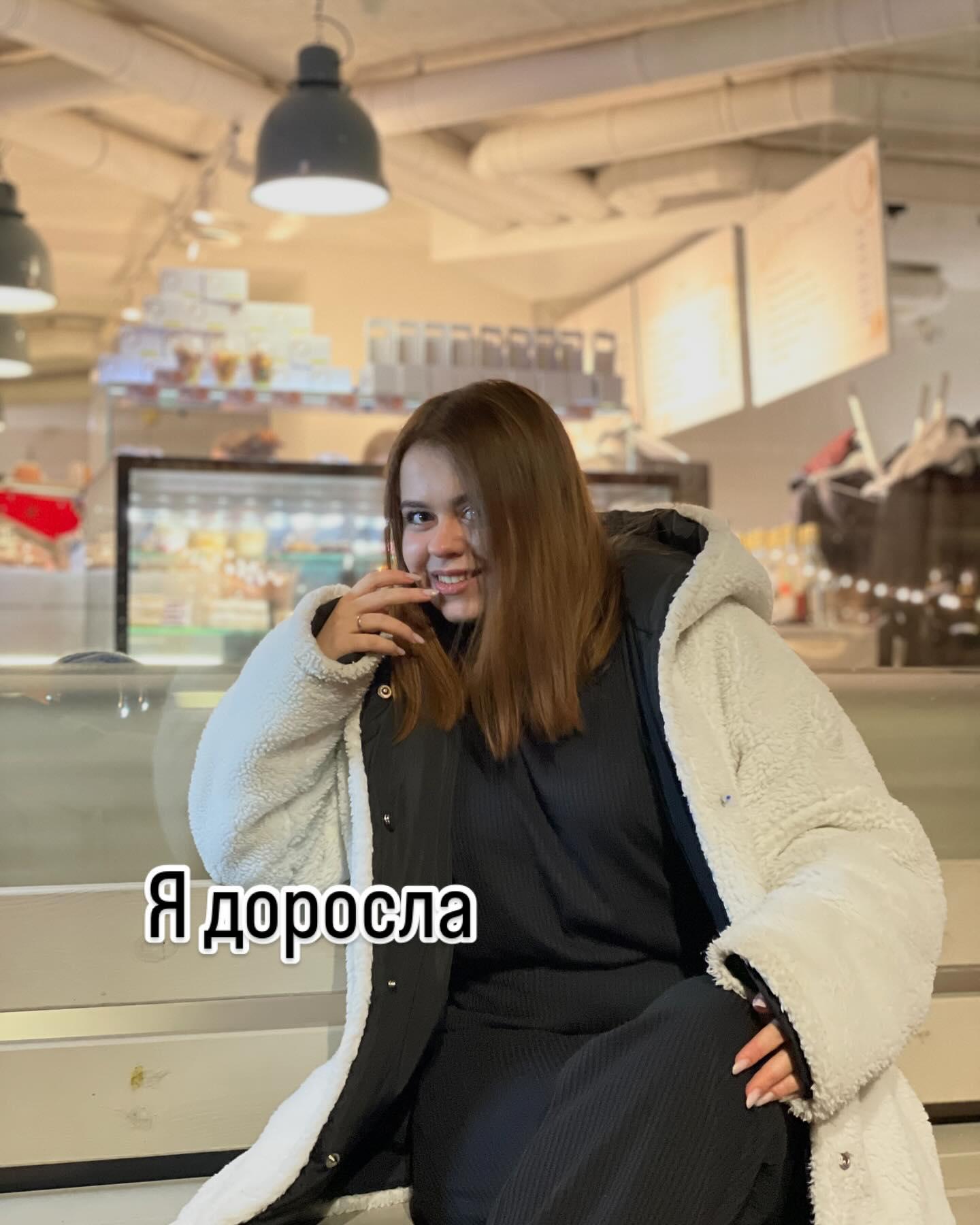 Марія Дерев'янченко в світлій шубці сидить у кафе; напис «Я доросла»
