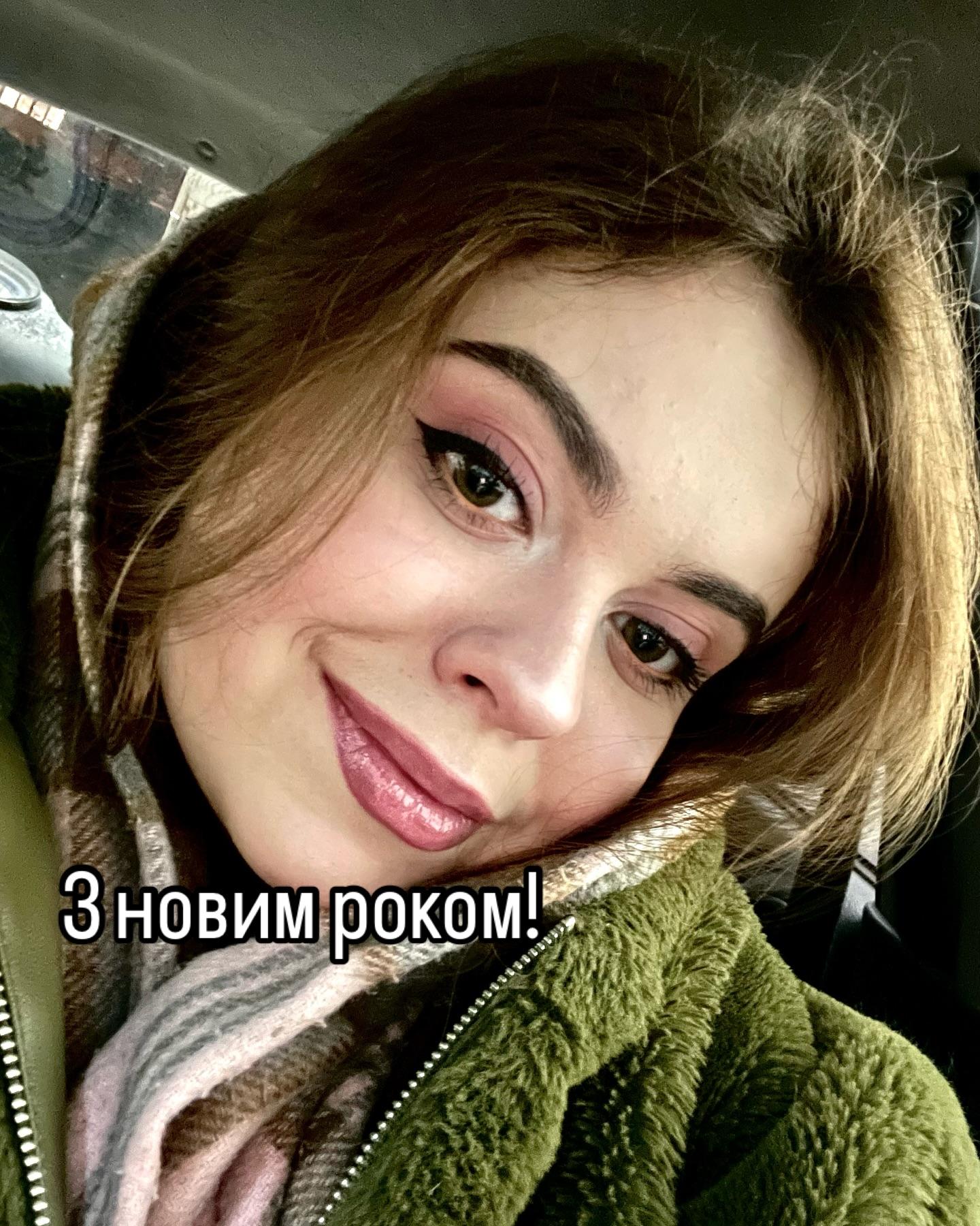 Усміхнена Марія Дерев'янченко в зеленій куртці та шарфі, селфі в авто; напис «З новим роком!»