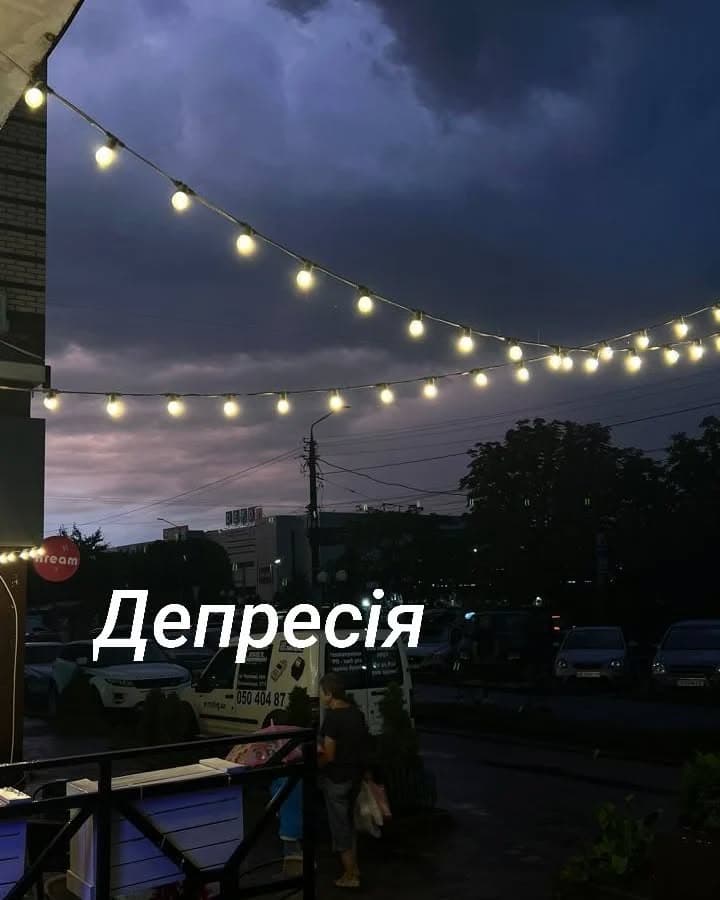 Вечірня вулиця під грозовим небом, над нею гірлянда з лампочок; напис «Депресія»