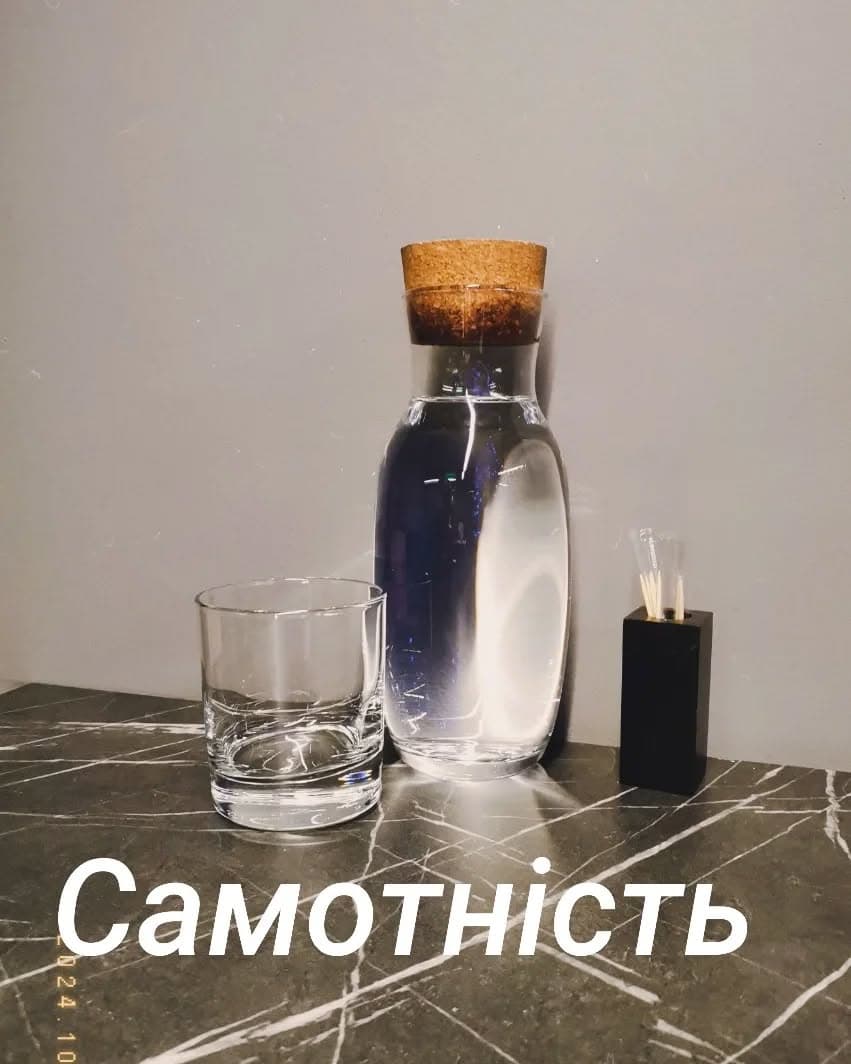 Скляний графин і порожня склянка на мармуровій стільниці; напис «Самотність»