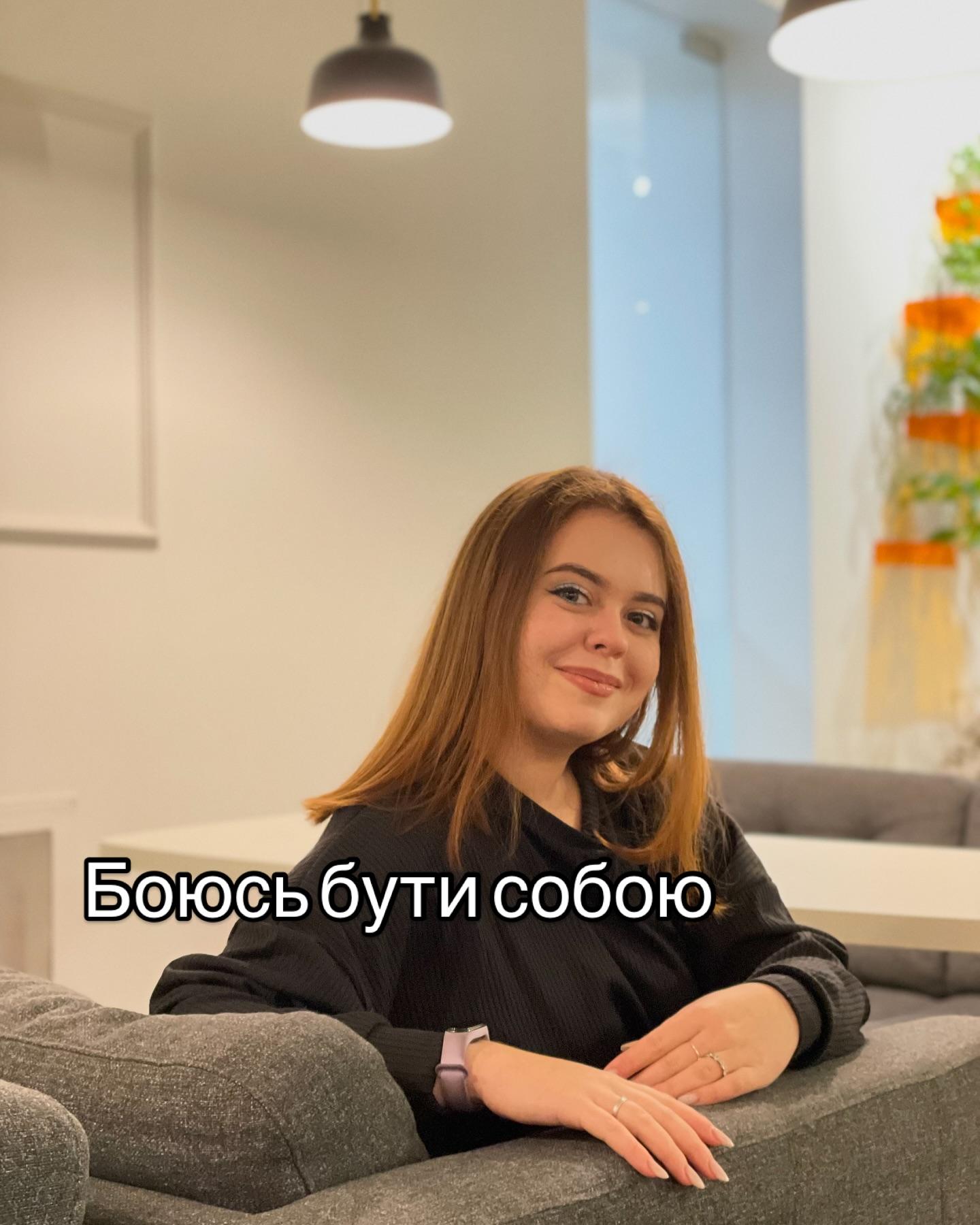 Марія Дерев'янченко сидить на сірому дивані у світлій кімнаті; напис «Боюсь бути собою»