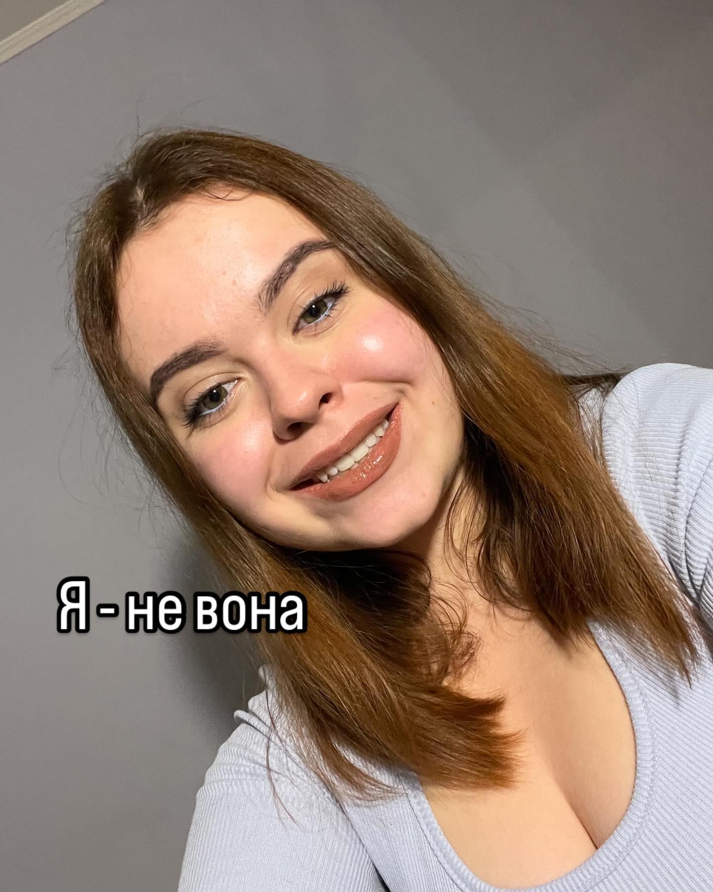 Усміхнена Марія Дерев'янченко на тлі світлої стіни; напис «Я - не вона»